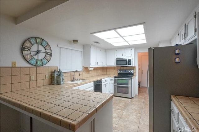 kitchen featuring a sink, tile countertops, appliances with stainless steel finishes, a peninsula, and decorative backsplash