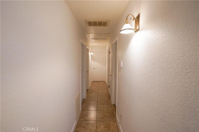 hallway with attic access, light tile patterned floors, a textured wall, and visible vents