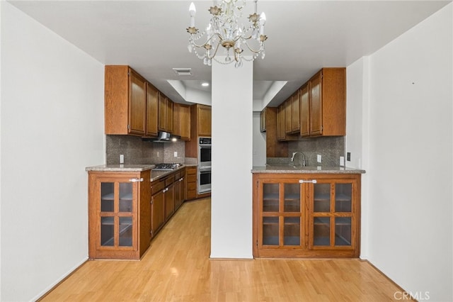 kitchen with light stone counters, backsplash, a chandelier, appliances with stainless steel finishes, and light wood-type flooring