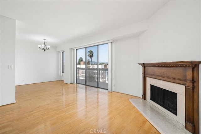 unfurnished living room with wood-type flooring, an inviting chandelier, and a premium fireplace