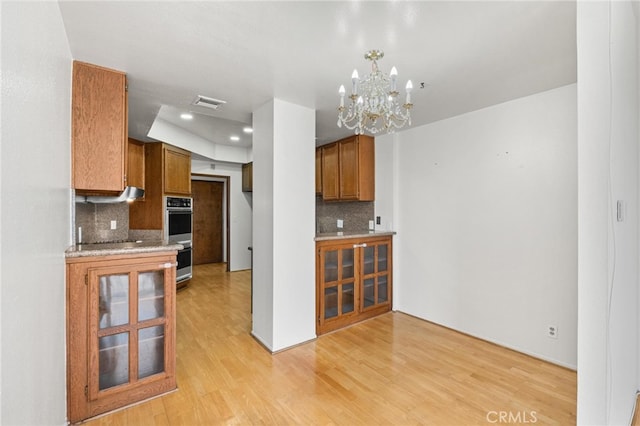 kitchen with decorative backsplash, light wood-type flooring, a chandelier, and double oven