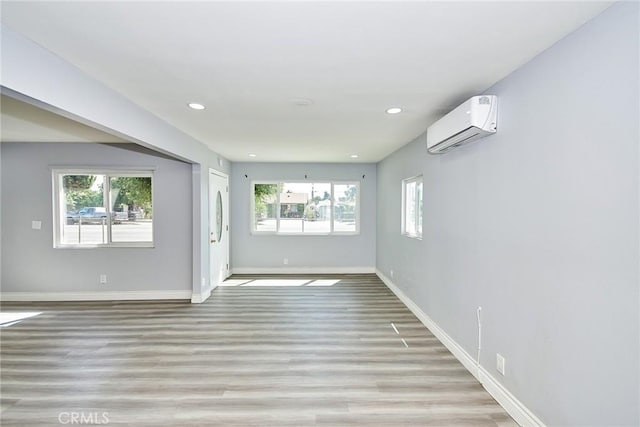 empty room with light wood-type flooring, a wall unit AC, and a wealth of natural light