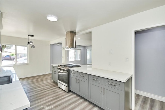 kitchen featuring island exhaust hood, gray cabinetry, light hardwood / wood-style flooring, stainless steel gas stove, and hanging light fixtures