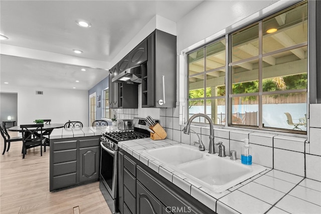 kitchen featuring light wood-type flooring, tasteful backsplash, stainless steel gas range, sink, and tile countertops