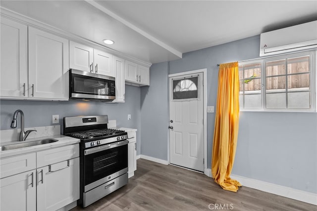 kitchen with a wall mounted air conditioner, appliances with stainless steel finishes, sink, dark hardwood / wood-style floors, and white cabinetry