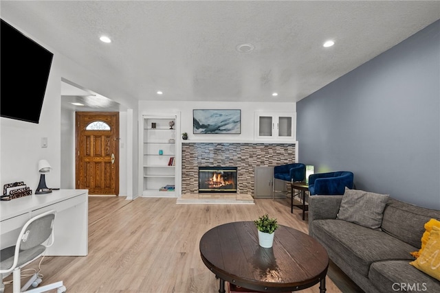 living room featuring built in shelves, a textured ceiling, light hardwood / wood-style floors, and a stone fireplace