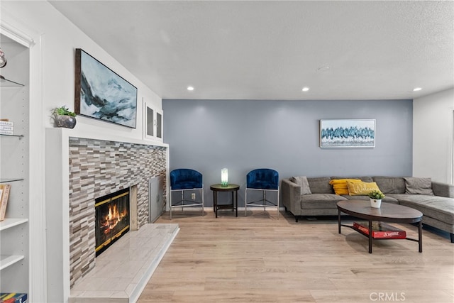 living room with a tile fireplace, a textured ceiling, and light hardwood / wood-style floors