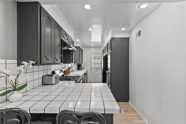 kitchen featuring light wood-type flooring, tasteful backsplash, stainless steel range, sink, and tile counters