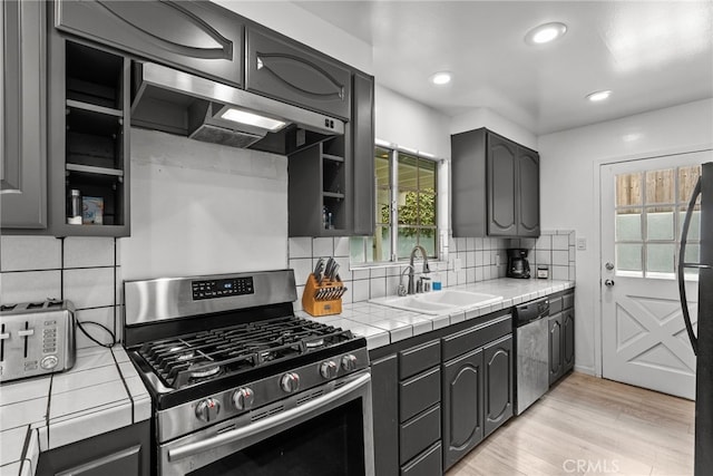 kitchen with sink, stainless steel appliances, backsplash, tile countertops, and light hardwood / wood-style floors