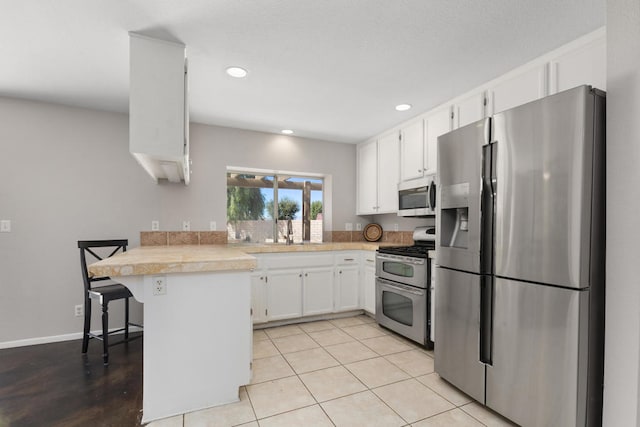 kitchen featuring light tile patterned floors, kitchen peninsula, white cabinetry, stainless steel appliances, and a breakfast bar