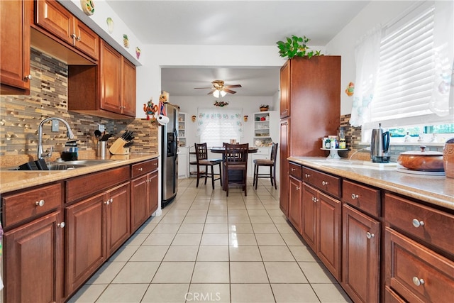 kitchen featuring light tile patterned flooring, sink, stainless steel refrigerator with ice dispenser, decorative backsplash, and ceiling fan