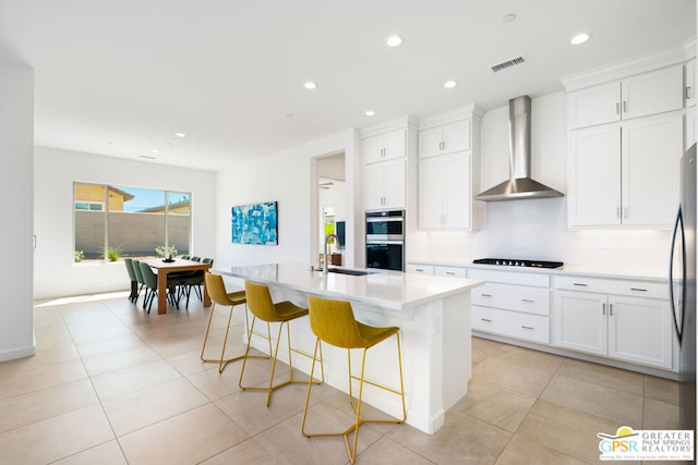 kitchen featuring sink, a center island with sink, white cabinetry, and wall chimney exhaust hood