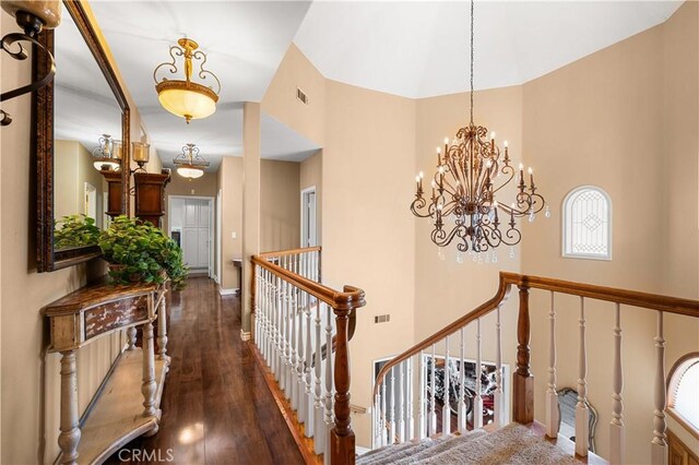 hall featuring a notable chandelier, wood-type flooring, an upstairs landing, a towering ceiling, and visible vents
