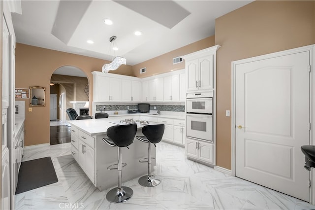 kitchen featuring decorative backsplash, a breakfast bar area, white cabinetry, pendant lighting, and white double oven