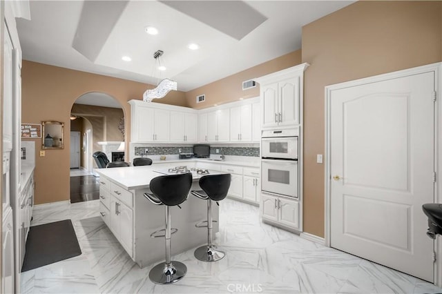 kitchen featuring decorative backsplash, a center island, arched walkways, light countertops, and white cabinetry