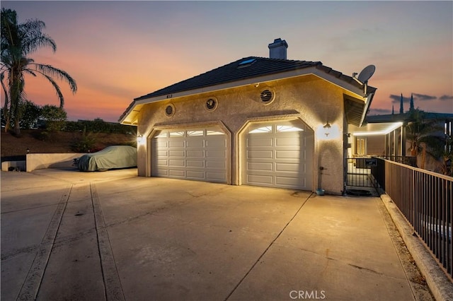garage at dusk with concrete driveway and fence