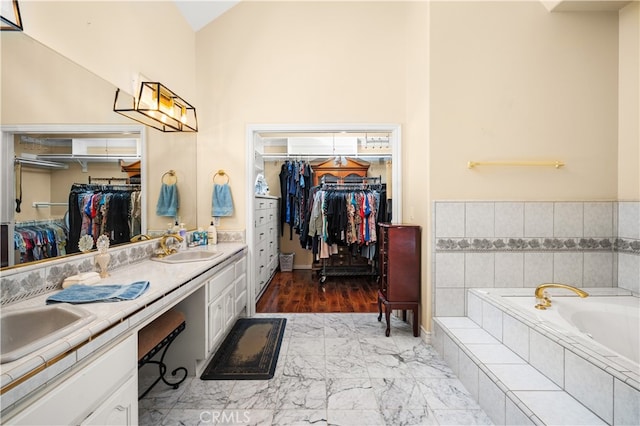 bathroom featuring vanity, a relaxing tiled tub, and high vaulted ceiling