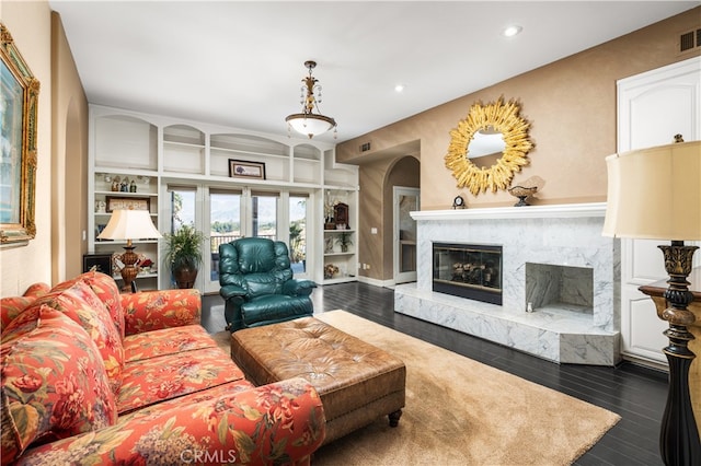 living room with a premium fireplace, dark wood-type flooring, and built in shelves