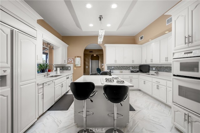 kitchen with white cabinetry, sink, a kitchen island, and white appliances