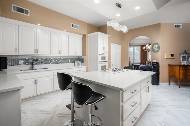 kitchen featuring white cabinets, tasteful backsplash, hanging light fixtures, a chandelier, and sink