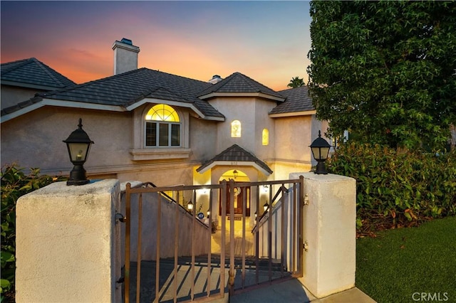 view of front of property with stucco siding, a fenced front yard, a gate, and a chimney