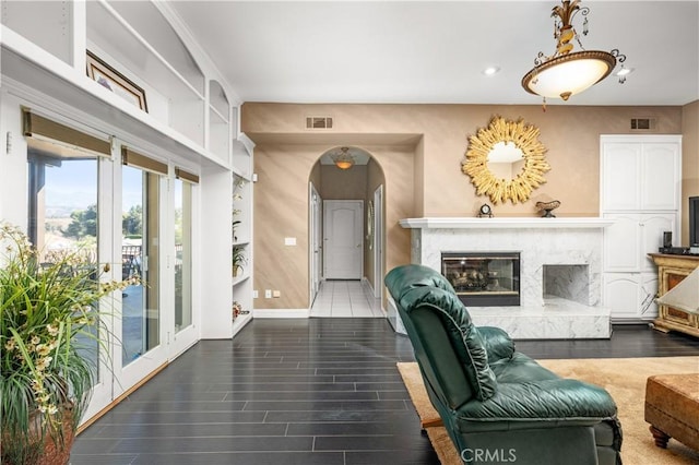 living room featuring visible vents, arched walkways, a fireplace, wood finished floors, and baseboards