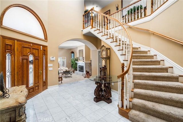 foyer entrance featuring stairs, arched walkways, a high ceiling, and baseboards