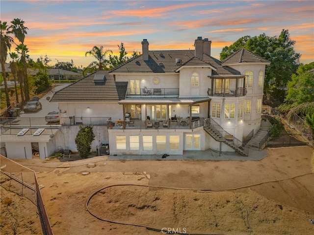 back house at dusk featuring a patio and a balcony