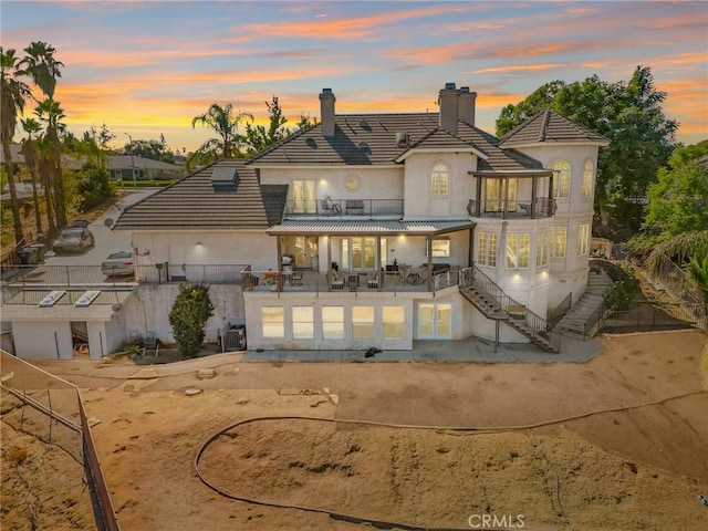 back of property featuring fence private yard, stucco siding, a balcony, and a chimney