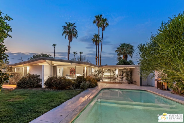 pool at dusk with a patio area and a lawn