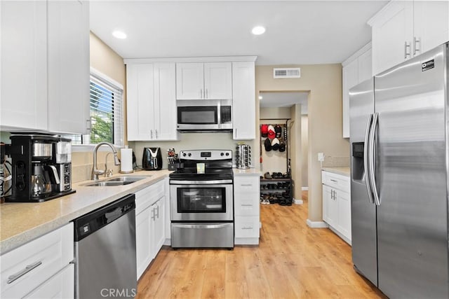 kitchen with white cabinets, sink, light hardwood / wood-style flooring, light stone countertops, and stainless steel appliances