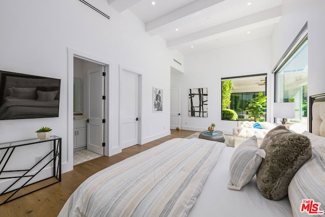 bedroom with beamed ceiling, a towering ceiling, dark wood-type flooring, and connected bathroom