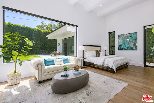 bedroom featuring multiple windows, beamed ceiling, and hardwood / wood-style flooring