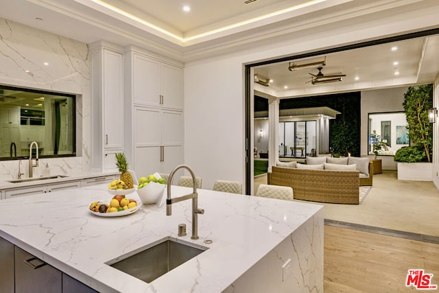 kitchen featuring white cabinets, a tray ceiling, light stone countertops, and sink