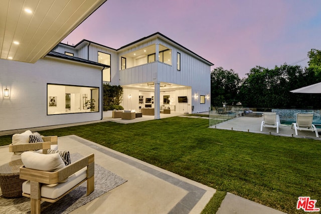 back house at dusk with an outdoor hangout area, a balcony, a pool, a yard, and a patio