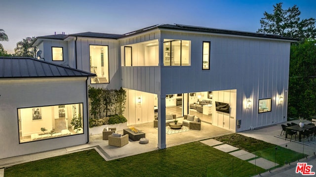 back house at dusk featuring a lawn, an outdoor living space with a fire pit, and a patio