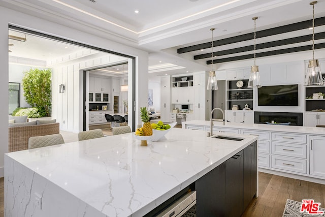 kitchen with pendant lighting, light stone countertops, beamed ceiling, and a large island with sink