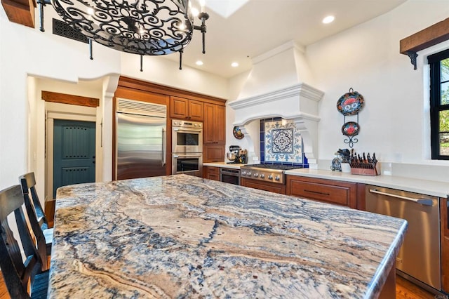 kitchen featuring appliances with stainless steel finishes, kitchen peninsula, light stone countertops, custom range hood, and light hardwood / wood-style flooring