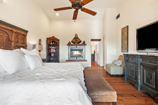 bedroom featuring ceiling fan, dark hardwood / wood-style floors, a multi sided fireplace, and a high ceiling