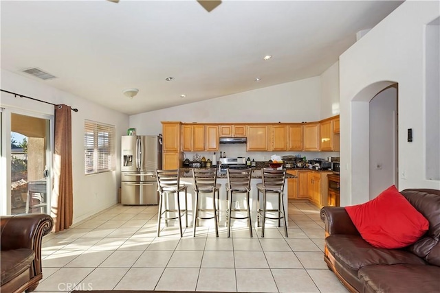 kitchen with high vaulted ceiling, an island with sink, a breakfast bar, light tile patterned floors, and appliances with stainless steel finishes