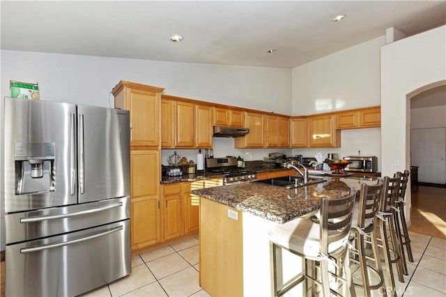 kitchen featuring sink, dark stone counters, a kitchen island with sink, light tile patterned floors, and appliances with stainless steel finishes