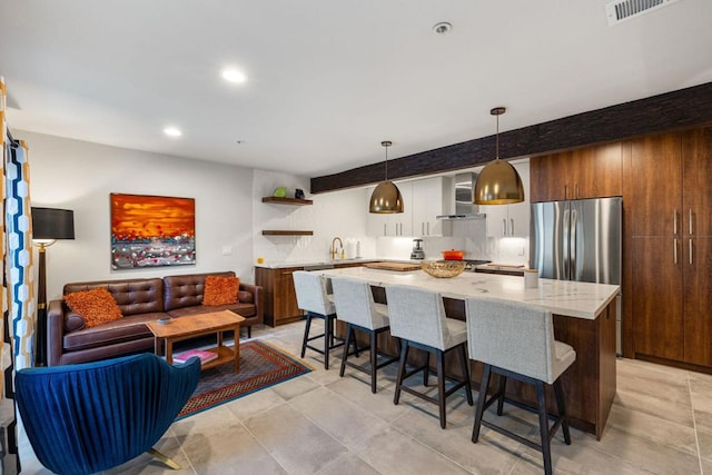 kitchen featuring decorative light fixtures, a kitchen island, wall chimney range hood, and a breakfast bar