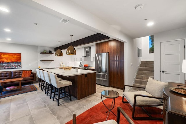 kitchen with wall chimney exhaust hood, stainless steel appliances, a kitchen breakfast bar, pendant lighting, and a kitchen island