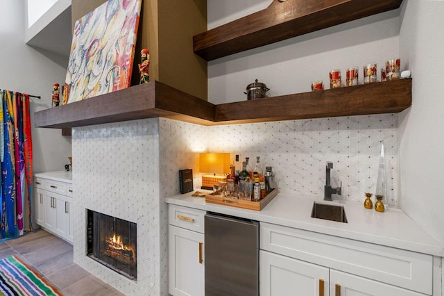 bar with stainless steel fridge, backsplash, white cabinetry, and sink