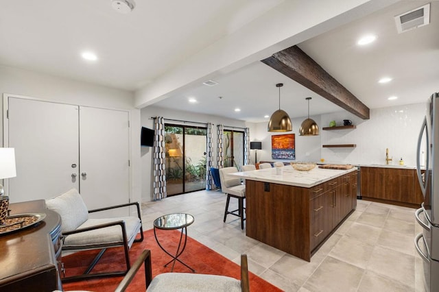 kitchen with dark brown cabinetry, pendant lighting, beamed ceiling, a center island, and stainless steel refrigerator