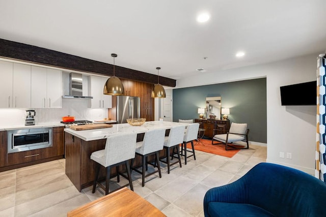 kitchen featuring a center island, wall chimney exhaust hood, hanging light fixtures, stainless steel appliances, and a kitchen breakfast bar