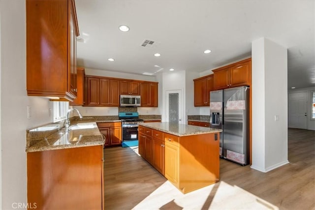 kitchen with sink, light hardwood / wood-style flooring, a kitchen island, and appliances with stainless steel finishes