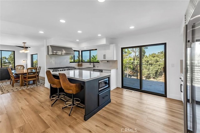 kitchen with sink, a kitchen island, pendant lighting, wall chimney range hood, and white cabinets