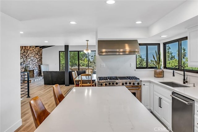 kitchen featuring sink, appliances with stainless steel finishes, white cabinetry, hanging light fixtures, and range hood