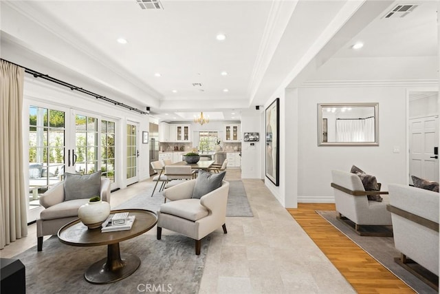 living room with french doors, light wood-type flooring, a tray ceiling, crown molding, and a chandelier